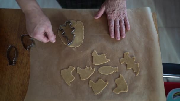 Close-up handen van vrouwelijke bakker maakt koekjes van deeg met behulp van een metalen mal. Zicht van bovenaf. Het deeg ligt op vetvrij papier. Zelfgemaakt koekjesrecept, traditioneel koken — Stockvideo