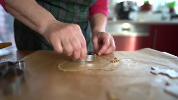 Zblízka ruce ženské pekařky dělá sušenky z těsta pomocí kovové formy. Těsto leží na nepromastitelném papíru. Domácí recept na sušenky, tradiční vaření — Stock video
