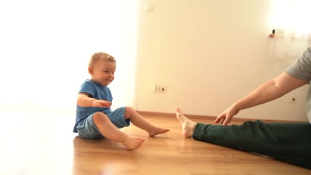 Een jonge vrouw en haar zoontje doen gymnastiek op de vloer thuis tijdens een covid-19 lockdown. stretching, grappige video kid herhaalt na mam — Stockvideo