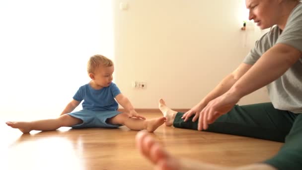 Hatha Yoga Fitness Mutter mit Baby. Eine junge Frau und ihr kleiner Sohn turnen zu Hause während einer Zwangspause auf dem Boden. Dehnendes, lustiges Videokind wiederholt nach Mama — Stockvideo
