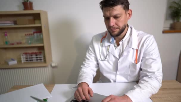 Telemedicine concept - male family doctor is talking to patient by laptop webcam and writing notes. Pulmonologist consults online, the new normality — Stock Video