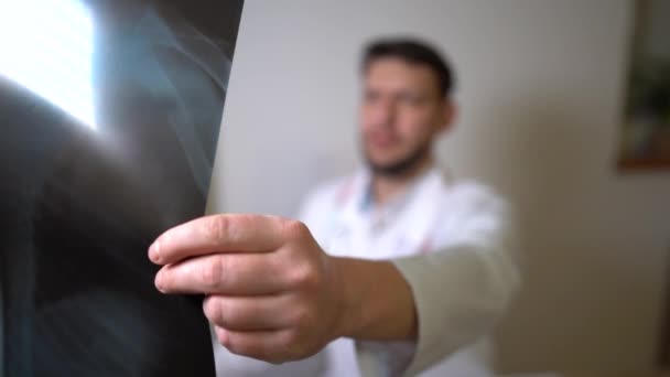El neumólogo examina cuidadosamente la imagen de rayos X del paciente. Primer plano de la mano y disparo. La cara de los médicos está borrosa. Hacer un diagnóstico durante la pandemia del coronavirus covid-19 — Vídeos de Stock