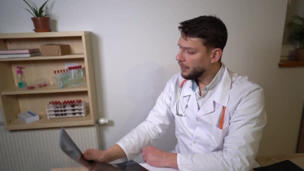 Lekarz informuje pacjenta o wynikach badań rentgenowskich. Pulmonolog umieszcza prześwietlenie pacjenta na stole. — Wideo stockowe