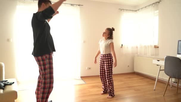 Rolig video far tränar sin dotter, flicka och far i pyjamas gör en rolig uppvärmning innan gymnastik. Fäder dag, stanna hemma — Stockvideo
