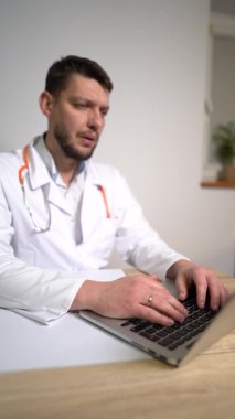 E-sağlık kavramı - erkek aile doktorunun dikey hâli, hastayla dizüstü bilgisayar kamerasıyla konuşmak ve notlar yazmak. Pulmonolog danışmanlık yapıyor, yeni normal...