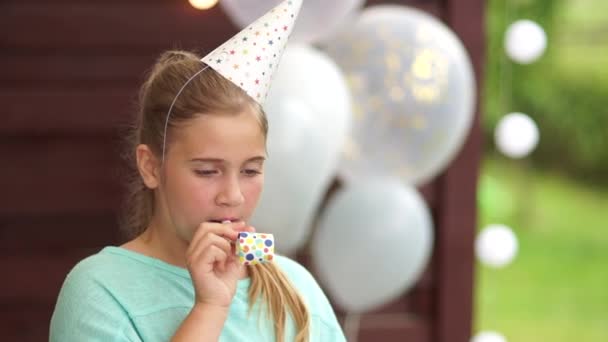 Feliz cumpleaños, retrato sobre un fondo de globos, cumpleaños de niños. Retrato de una chica con cuerno de fiesta soplando en sopladores — Vídeos de Stock