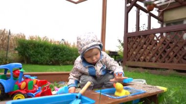 Soğuk havada kum havuzunda tatlı bir çocuk. Küçük çocuk dışarıda kumsalda oyuncak oynuyor. Mutlu çocukluk, çocukların eğlencesi.