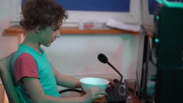 Apuestas adicción y el concepto de adolescentes. El adolescente juega un juego de red de computadoras y come mientras está sentado en la mesa — Vídeo de stock