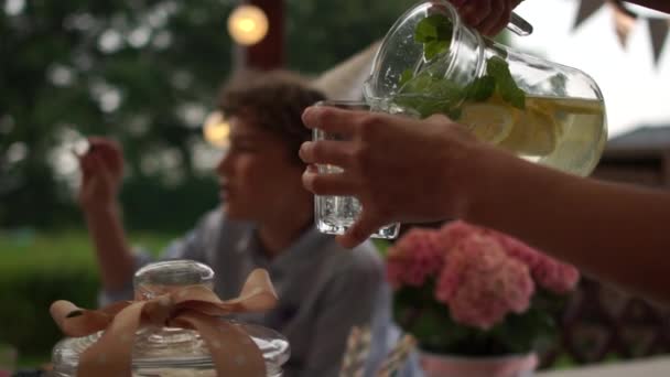 Egy közeli nő, aki limonádét önt az üvegbe. Egy csapat tinédzser, akik szabadtéri szülinapi bulit tartanak. Gyermek születésnap szabadtéri, vendéglátás koncepció — Stock videók