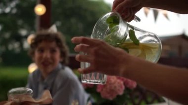 Bir grup ergen dışarıda doğum günü partisi veriyor. Çocukların doğum günü açık havada, yemek servisi konsepti. Yakın plan kadın cama limonata döküyor.