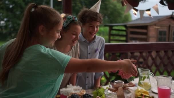 Drie gelukkige vrienden staan rond de verjaardagstafel. Catering concept, kinderen verjaardagsfeest — Stockvideo