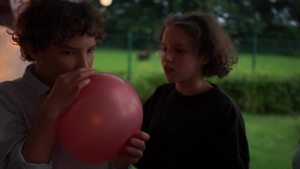 Egy fiú és egy lány héliummal teli lufit tart a kezében. Lélegezz a levegőbe, és beszélj halkan. Vicces videó, jó szórakozást. — Stock videók