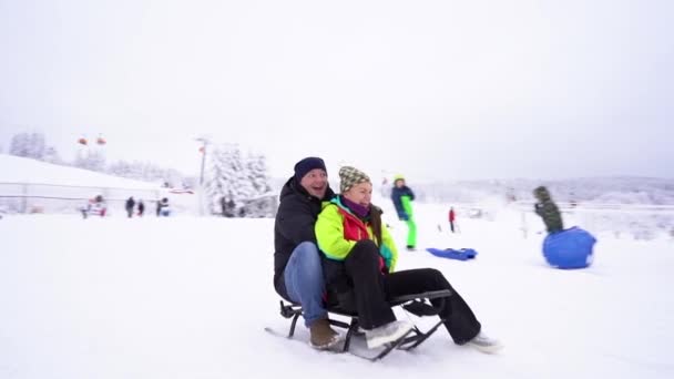 Portretul unei tinere şi al unui tânăr care săniuieşte pe zăpadă. O familie fericită se odihnește într-o stațiune de schi, săniuind pe munte — Videoclip de stoc