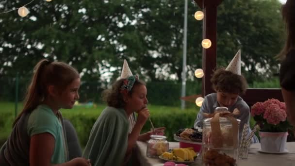 Groupe d'adolescents ayant une fête d'anniversaire en plein air. Anniversaire des enfants en plein air, concept de restauration. Enfants joyeux manger des baies tout en étant assis à la table festive — Video