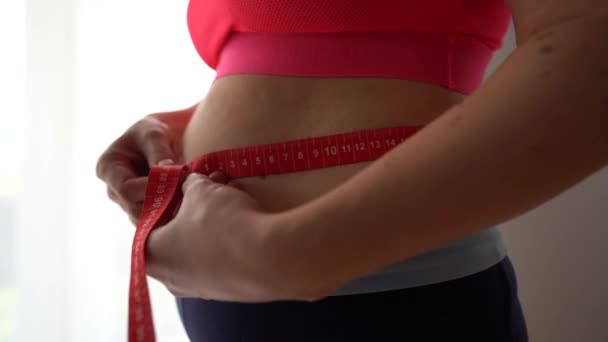 Close up de uma mulher grávida em um traje de treino medindo a circunferência de sua barriga com uma fita métrica. Monitorização da gravidez — Vídeo de Stock