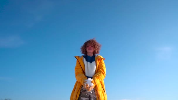 Зимний портрет кудрявой девочки-подростка. Счастливая девушка бросает снег и вращается против голубого неба — стоковое видео