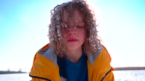 Retrato de inverno close-up de uma menina encaracolada contra um céu azul. Cabelo de meninas coberto de neve, conceito de felicidade de férias de inverno — Vídeo de Stock
