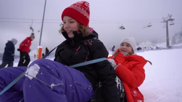 Menina enyoing passeio deslizante na neve. Happy teen girls deslizando para baixo da colina no trenó. Infância feliz, pista de esqui — Vídeo de Stock