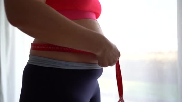 Young woman measures her waist with a tape measure, close-up. The girl is unhappy with her figure, postpartum depression — Stock Video