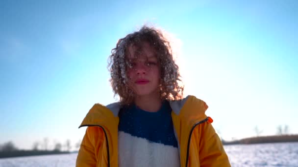 Winterportret van een meisje in een gele jas tegen de blauwe lucht. Er is sneeuw in de meisjes haar — Stockvideo