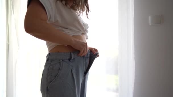 Young woman tries to button up jeans on her belly, which is plump after childbirth. Bodypositive concept — Stock Video