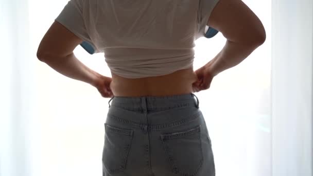 Vista traseira. Close-up de depósitos de gordura na cintura. Menina em jeans de tamanho pequeno, pendurado nas laterais — Vídeo de Stock
