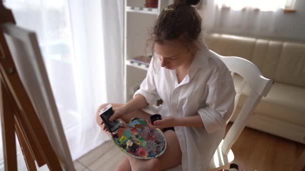 Krásná dívka umělec mačkat barvy na paletě chystá malovat na plátno. Koncept hobby a umění — Stock video