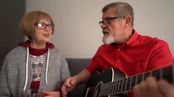 Portret starszej pary cieszącej się grą na gitarze we własnym domu. Mają uśmiechniętą i szczęśliwą twarz. Koncepcja aktywności wieku emerytalnego — Wideo stockowe