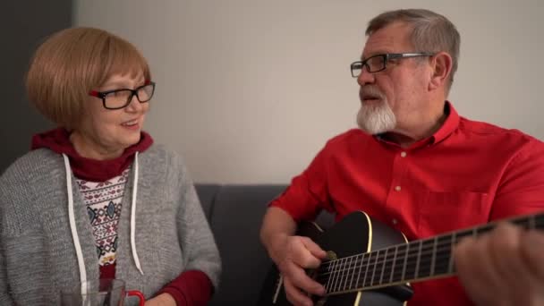 Ehemalige Eheleute verbringen das Wochenende zusammen. Ein Mann im roten Hemd spielt eine Akustikgitarre und eine Frau singt. Aktiv im Alter, zu Hause bleiben. Glückliches reifes Paar — Stockvideo