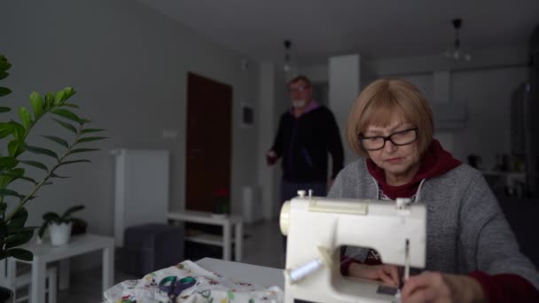 Vårdande make tog med te till sin fru medan hon arbetar med symaskinen. Äldre par, stanna hemma, favorit hobby, familjeföretag — Stockvideo