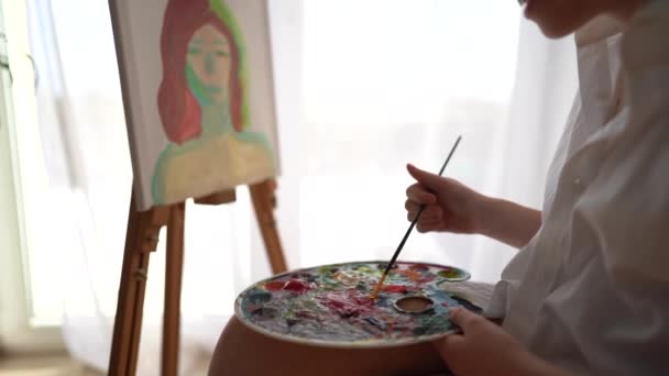 少女のクローズアップは、油絵具でキャンバスに描画し、パレットにそれらを攪拌します。趣味や芸術、子供のレジャー — ストック動画