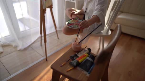 Schattig schoolmeisje is bezig met creativiteit thuis. Het meisje schildert een schilderij op doek. Blijf thuis concept — Stockvideo