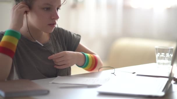 Liseli kız bir ders kaydeder ve bir görevi defterde tamamlar. Kıvırcık saçlı bir kızın yakın portresi internetten bilgisayar ve kulaklık kullanarak ders alıyor. — Stok video