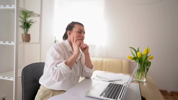 La mujer de negocios con una camisa blanca está hablando en video comunicación en la oficina. Videollamada con socios, ella sostiene el micrófono y habla — Vídeo de stock