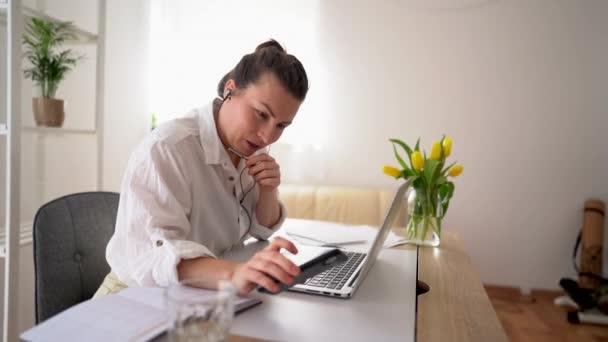 Donna d'affari multitasking in camicia bianca nel suo ufficio. Videochiamata con i partner, tiene il microfono e parla, controlla il telefono — Video Stock