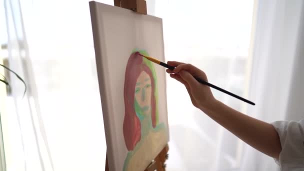 Close-up portrait on canvas by a childs hand. Girl draws while sitting at the easel in the studio, childrens creativity — Stock Video