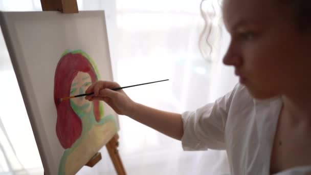 Portred de la fille peignant un tableau. Une écolière apprend à dessiner. Adolescente dessine un autoportrait assis sur une chaise près de la fenêtre — Video