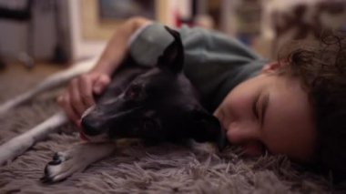 Yerde yatan yaramaz bir genç çocuk köpeğine sarılıyor. Oğlan ve onun siyah beyaz melezi, çocuk ve köpek