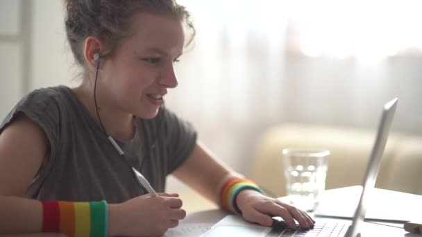 Chica adolescente de pelo rizado hace la tarea cerca de la computadora portátil. Aprendizaje en línea, aprendizaje a distancia, educación en el hogar — Vídeo de stock