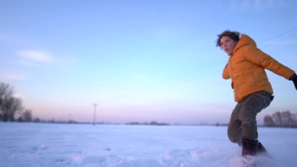 Niño adolescente en una chaqueta de invierno juega bolas de nieve en un campo cubierto de nieve. Actividad invernal, infancia feliz — Vídeos de Stock