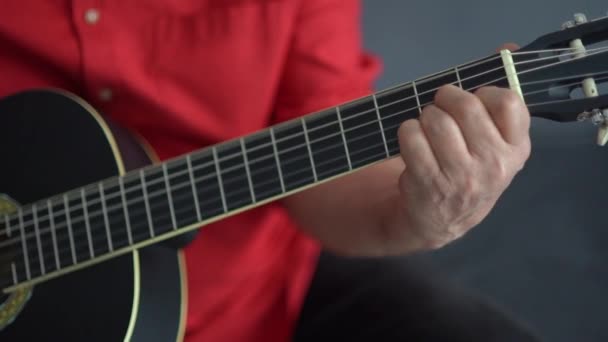 Close-up de um homem idoso com uma camisa vermelha fazendo seu hobby favorito, tocando uma guitarra acústica. Lição de guitarra — Vídeo de Stock