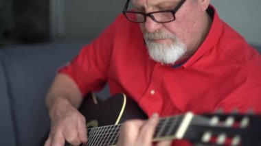 Kırmızı gömlekli ve gözlüklü yaşlı bir adam akustik gitar çalar. En sevdiği hobi, gitar çalmayı öğrenmek, evde kalmak.