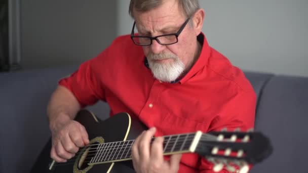 Zblízka dospělý muž v červené košili a brýle hraje na akustickou kytaru. Oblíbený koníček, naučit se hrát na kytaru, zůstat doma — Stock video