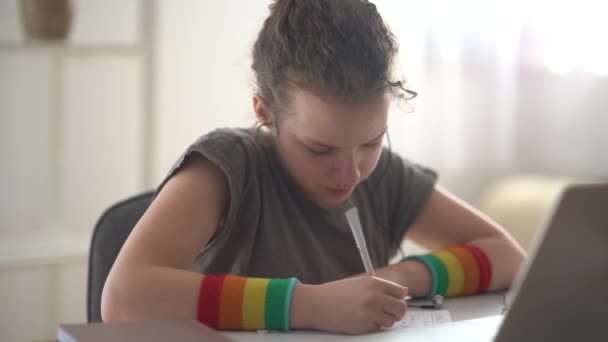 Chica adolescente de pelo rizado hace la tarea cerca de la computadora portátil. Aprendizaje en línea, aprendizaje a distancia, educación en el hogar — Vídeo de stock