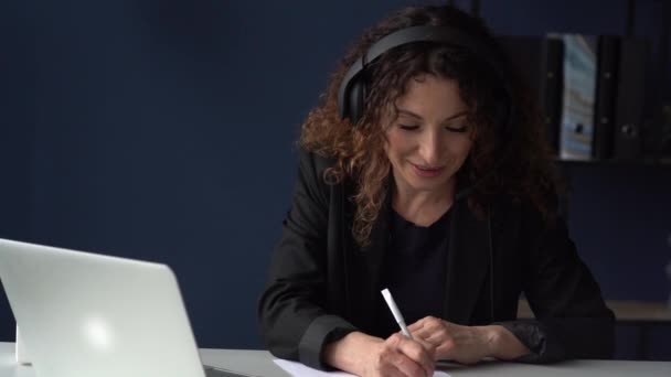 Poważne skupione kobieta biznesu ze słuchawkami za pomocą laptopa podczas rozmowy wideo. Praca zdalna podczas koronawirusu. Młoda kobieta na stanowisku — Wideo stockowe