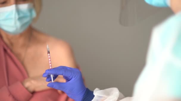 한 여성 의사가 코로나 바이러스 (COVID-19 면역 체계 ) 를 만들기 위해 보호용 마스크를 쓰고 있는 백발의 여성을 위해 백신을 준비하고 있습니다. — 비디오