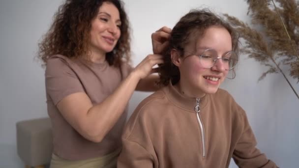 Bonito carinhoso cabelos encaracolados mãe tranças suas filhas adolescentes tranças. Mãe e filha — Vídeo de Stock