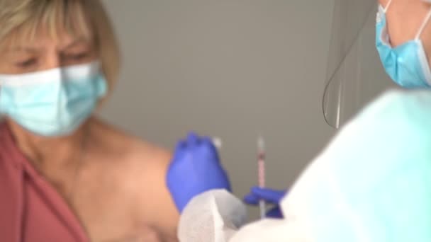 Läkare som vaccinerar gamla patienter på kliniken med kopieringsutrymme. Läkaren ger injektioner till en äldre kvinna på sjukhuset. Sköterska som håller sprutan före framställningen av Covid-19 eller coronavirus vaccin — Stockvideo