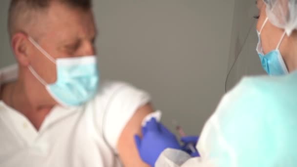 시니어 시민 이 백신을 기다리고 있습니다. 얼굴에 마스크를 쓴 의사가 성숙 한 남자에게 총을 쐈어요. 파란색 비디오, 백신으로 된 인슐린 주사기에 집중하 세요. — 비디오