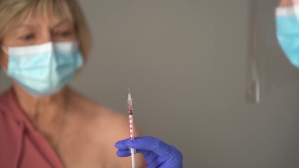 Концепція вакцинації проти кодоїдів-19 . Крупним планом портрет літнього пенсіонера і шприца з дозою вакцини, зріла жінка готується отримати вакцину — стокове відео